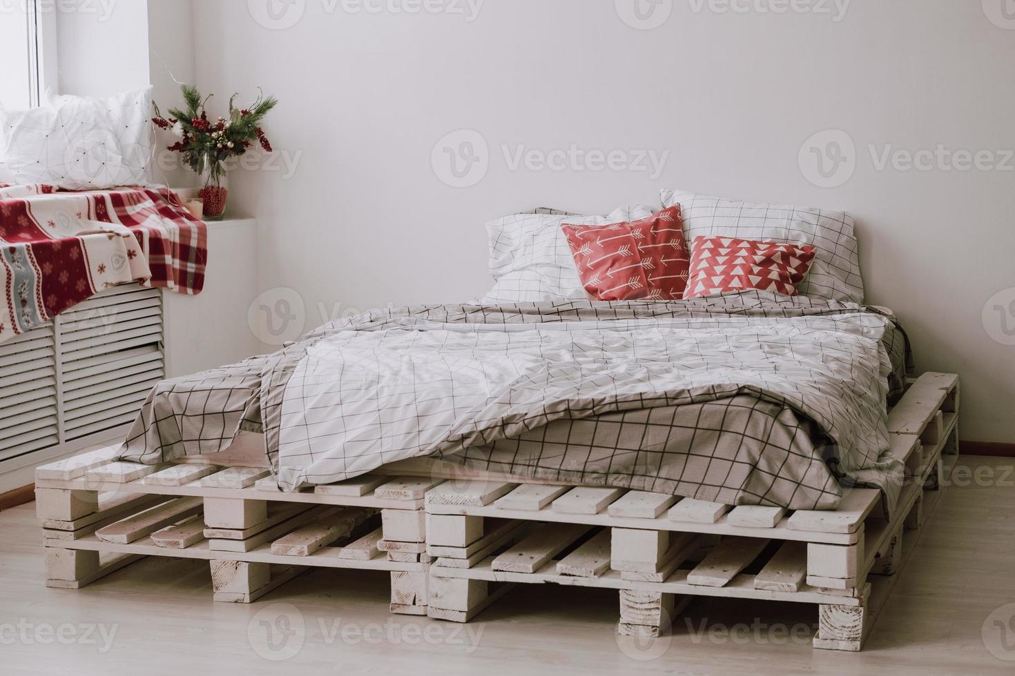 homemade bed made of pallets by the window with Christmas decorations. Cozy corner in the bedroom photo