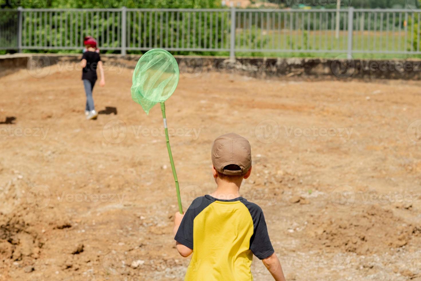 niño pequeño caminando por el campo con una red en el verano. red verde brillante en manos de un niño. estado de ánimo de verano. camiseta amarilla. infancia feliz en vacaciones de verano foto