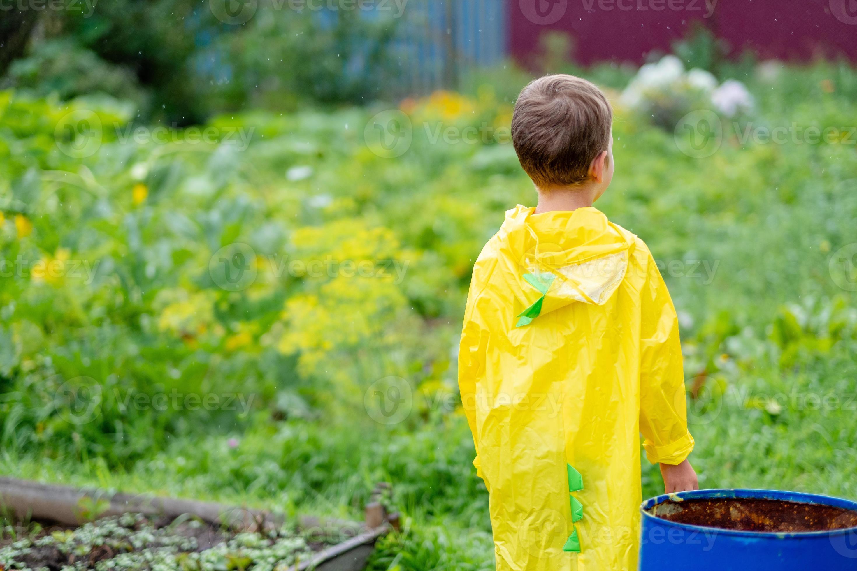 A boy in a yellow raincoat walks in the rain, back view. A child on the