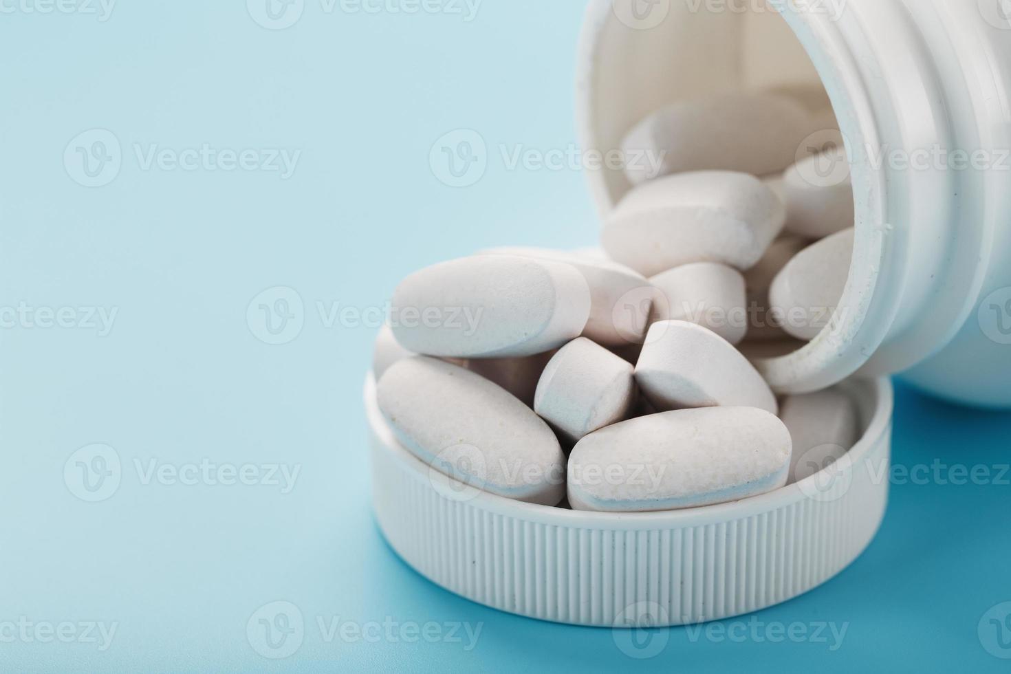 Vitamins and minerals in white capsules fell out of a white jar on a blue background. photo