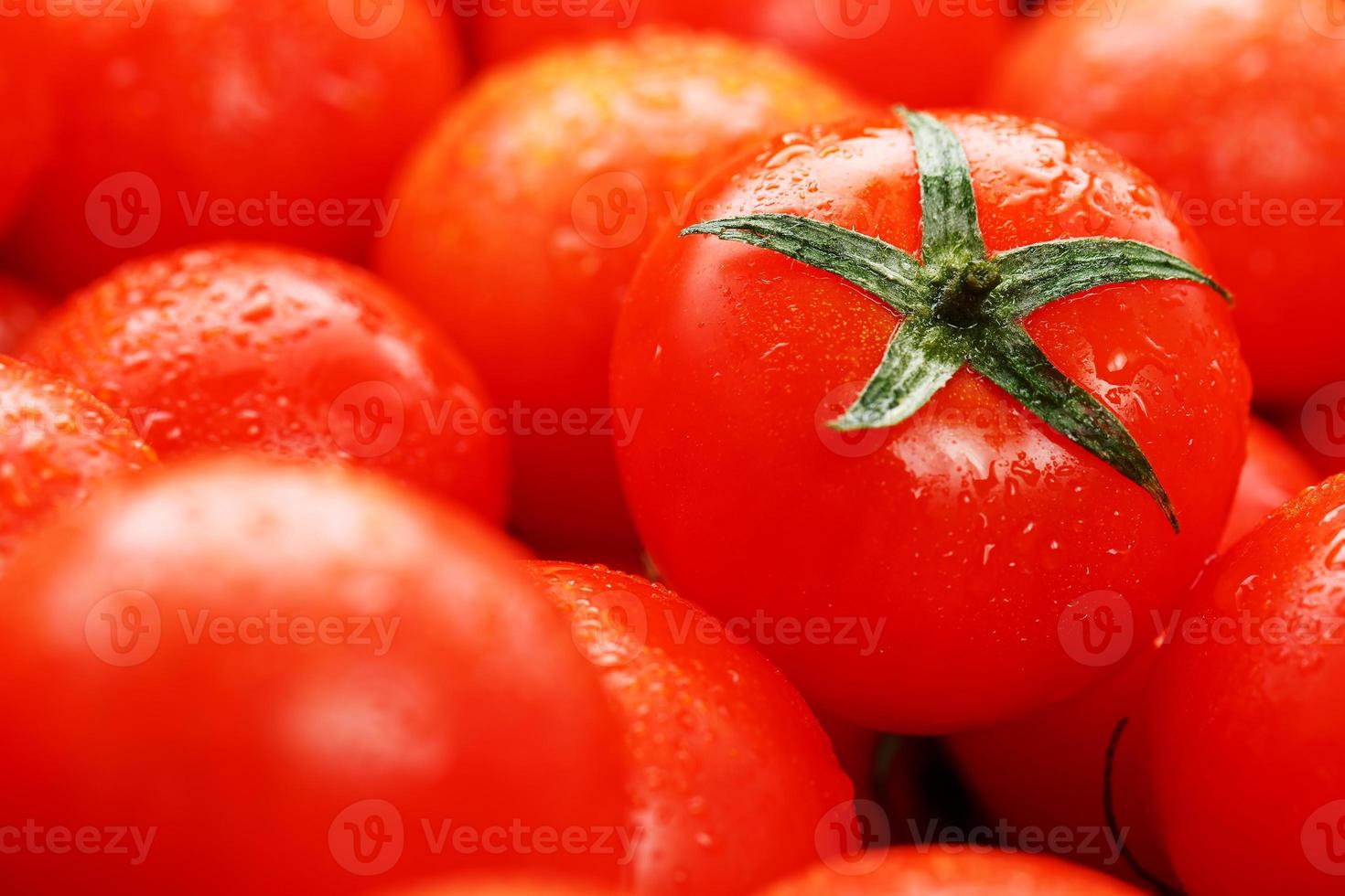 Ripe red tomatoes, with drops of dew. Close-up background with texture of red hearts with green tails. Fresh cherry tomatoes with green leaves. photo