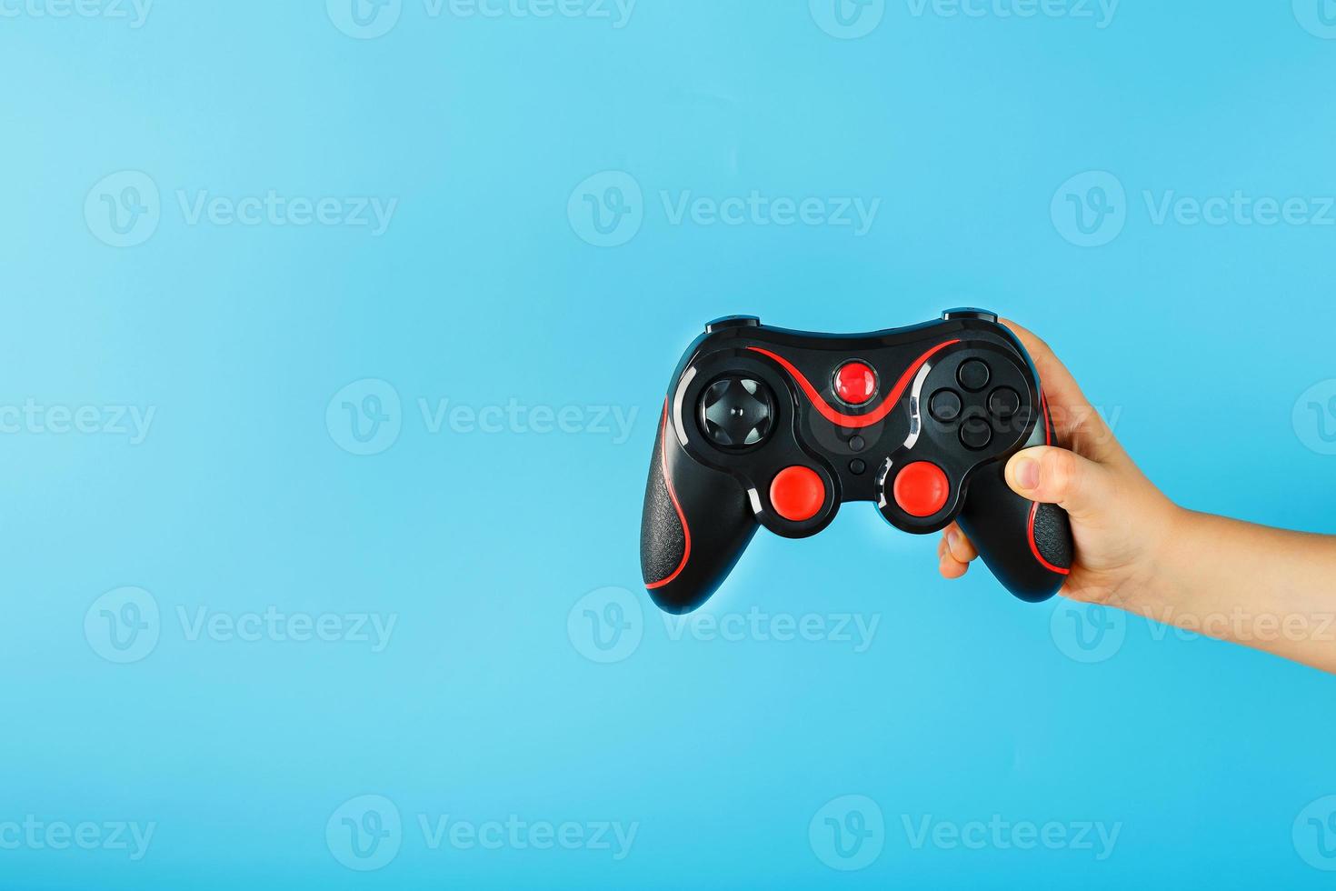 A child's hand triumphantly holds the gamepad on a blue background. Clear space photo