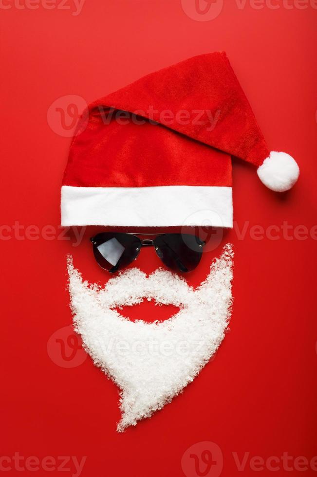 Santa Claus Hat and beard made of snow with black glasses on red background. photo