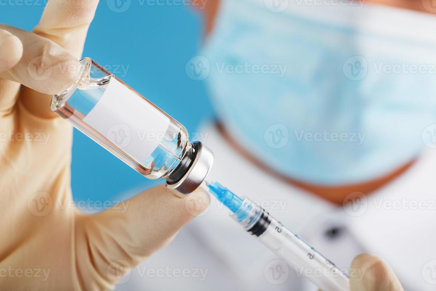 un médico con guantes de goma sostiene una ampolla con una vacuna y una jeringa, de cerca. foto