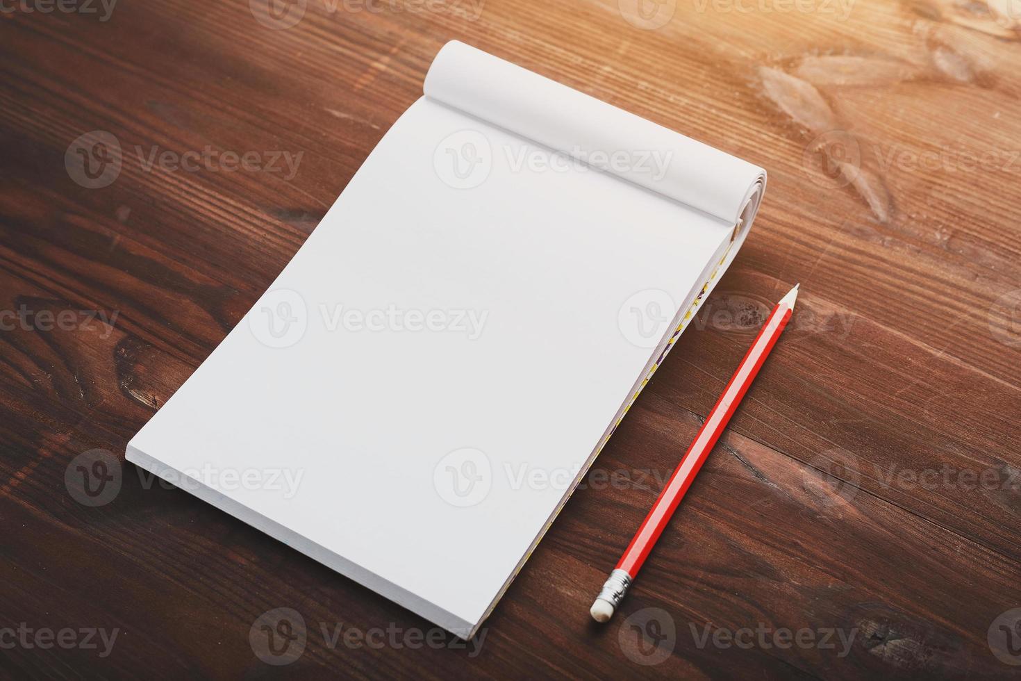 Notebook with a red pencil on a brown background with warm sunlight, for writing. Free empty space for writing on a blank sheet of a notebook. photo