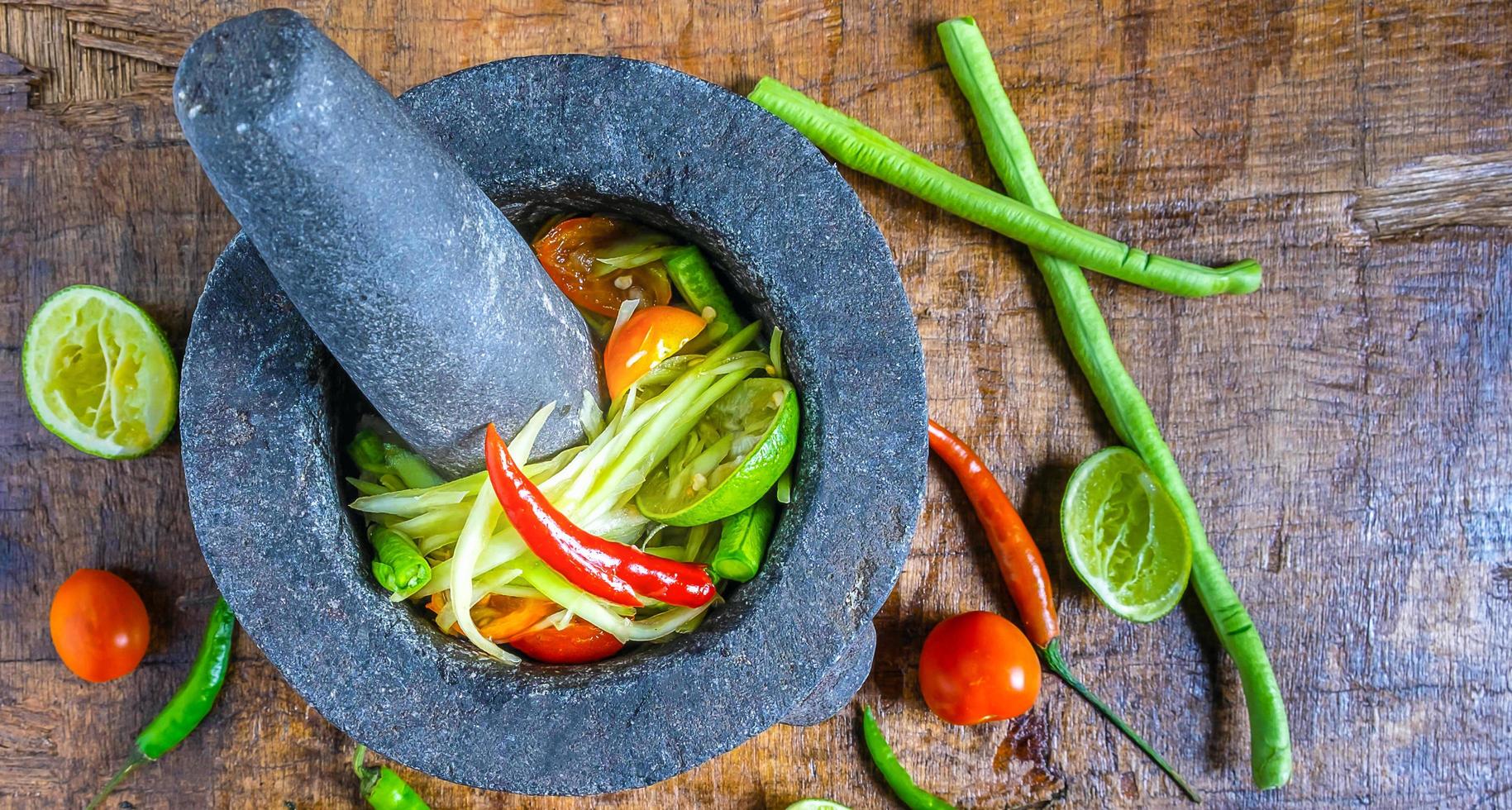 Cooking of menu Thai food papaya salad on with lemon and tomato on a wooden background.Top view photo