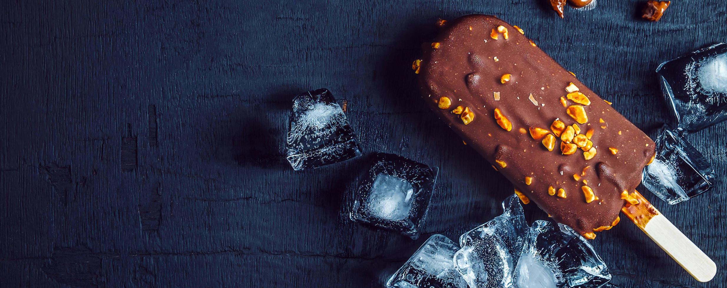 A delicious chocolate ice cream bar with almonds and ice cubes is placed on a black background.Top view photo