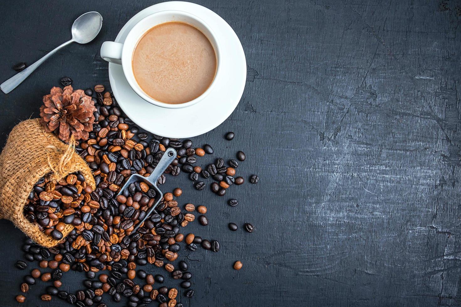 vista superior de una mezcla de tostado oscuro y un tostado medio de granos de café tostados en una bolsa de saco marrón con una taza de café caliente foto