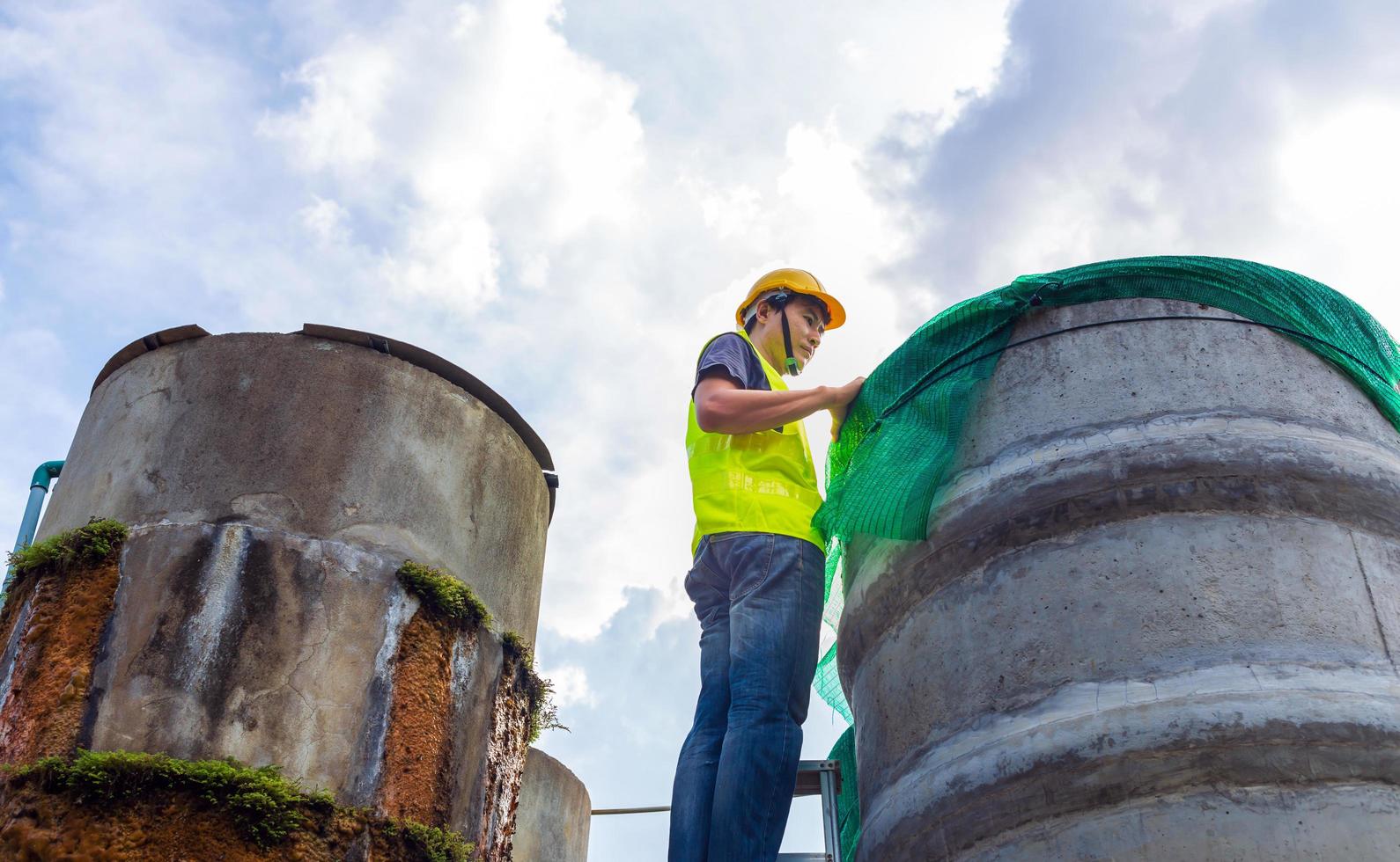 engineer controlling the quality of water Stand on the risky stairs at high places operating industrial water purification or filtration equipment old cement tanks for keeping water in water factory photo