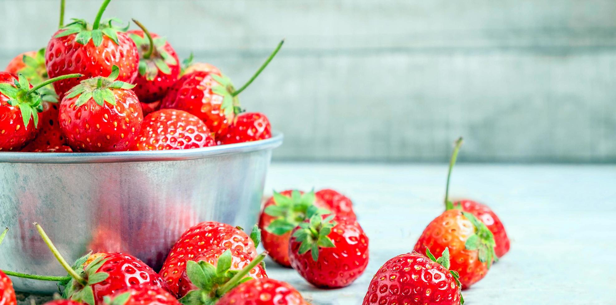 primer plano de fresas rojas frescas en un recipiente sobre un fondo azul de madera vieja foto