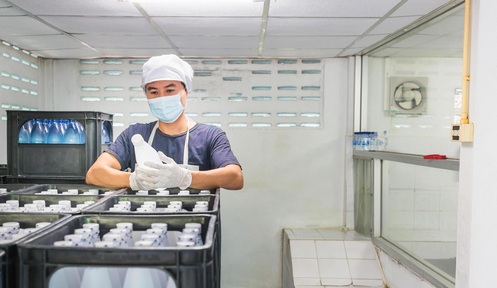 Young man worker or quality inspector in workwear and with a protective mask on his face working in checking bottled drinking water in drink water factory before shipment.drinking water business photo