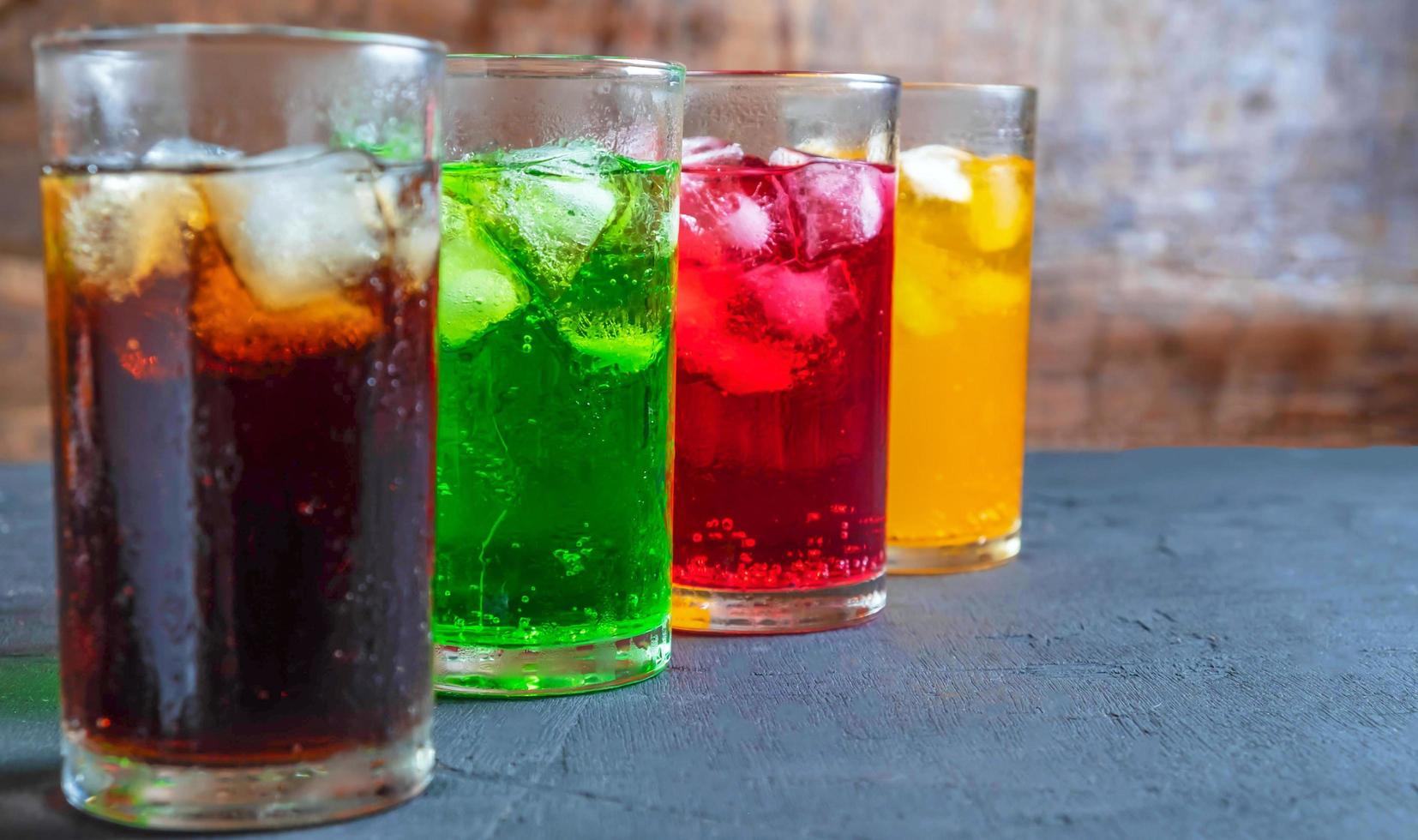 un montón de refrescos en vasos coloridos y sabrosos sobre la mesa,vasos con bebidas dulces con cubitos de hielov foto