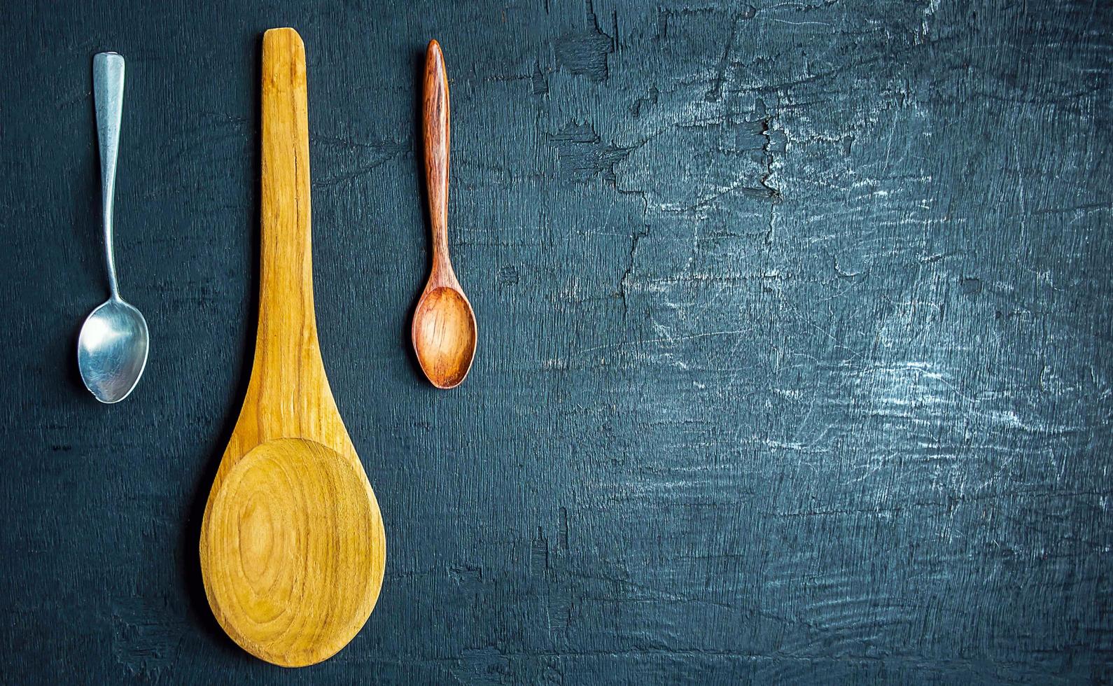 colección de cucharas grandes de madera con cucharas pequeñas y de acero inoxidable sobre fondo negro, vista superior. foto