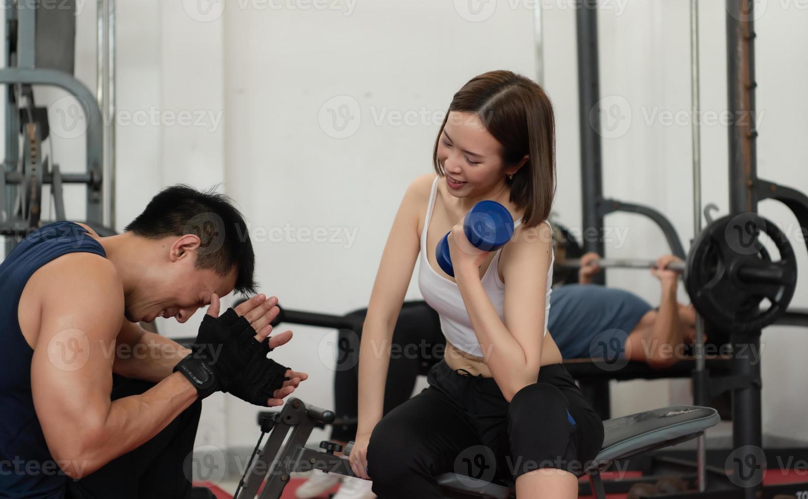 Young couple exercising in a gym When lifting weights, they assist one another. Concept of bodybuilding and healthy living photo