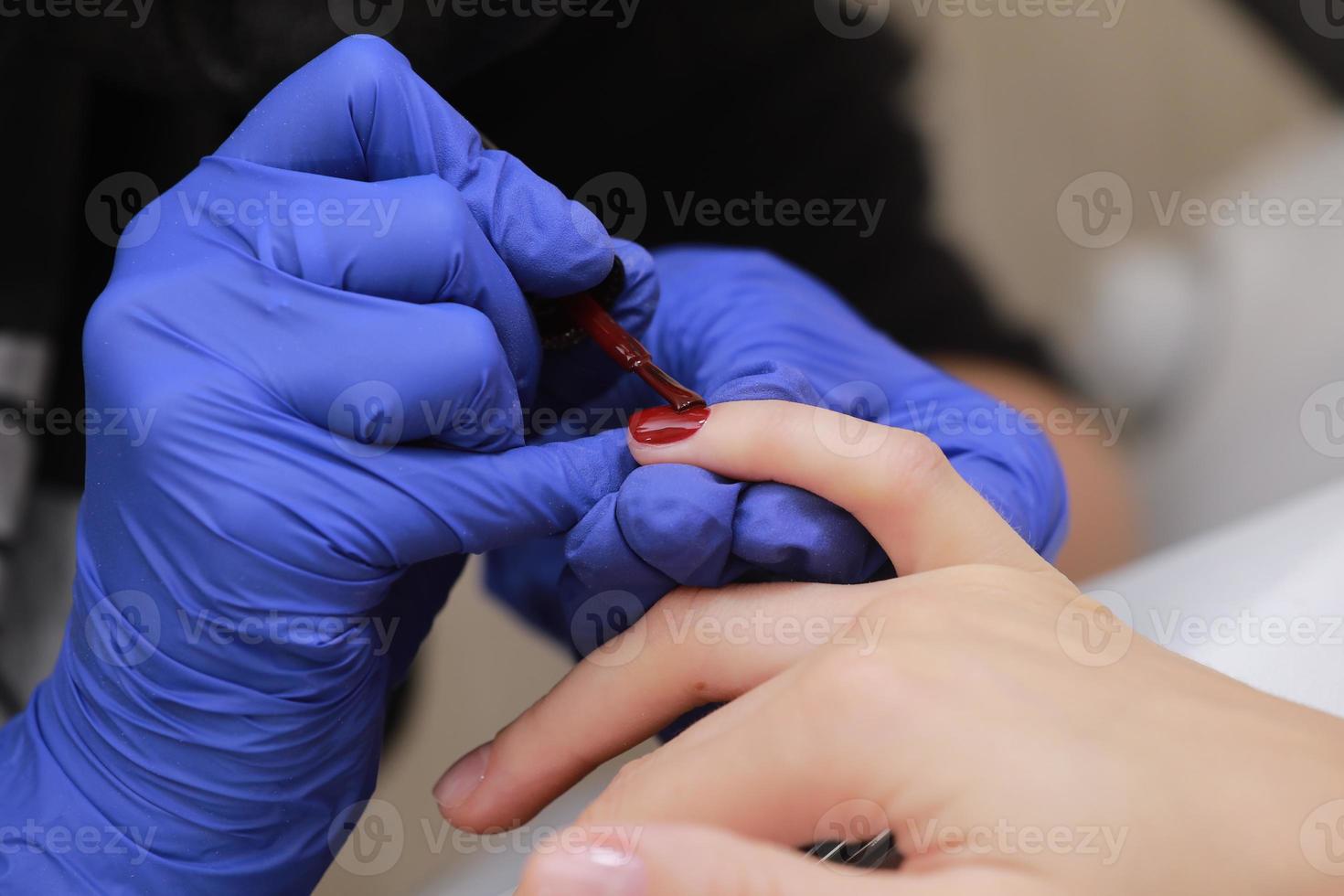 Master in protective gloves during a manicure at beauty salon. Master manicurist varnishes the marsala gel on the nails of a female client. The concept of beauty and health. photo