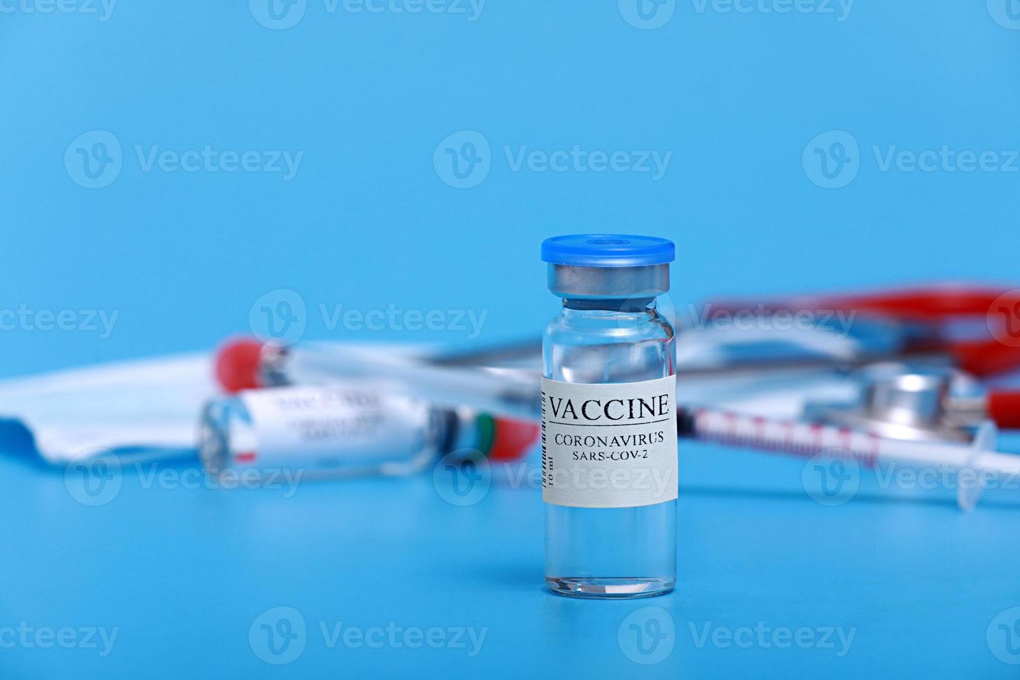 vial médico con vacuna contra el coronavirus covid-19, jeringa, estetoscopio y mascarilla facial sobre fondo azul con espacio de copia. sesión de vacunación y mejora de la inmunidad. foto