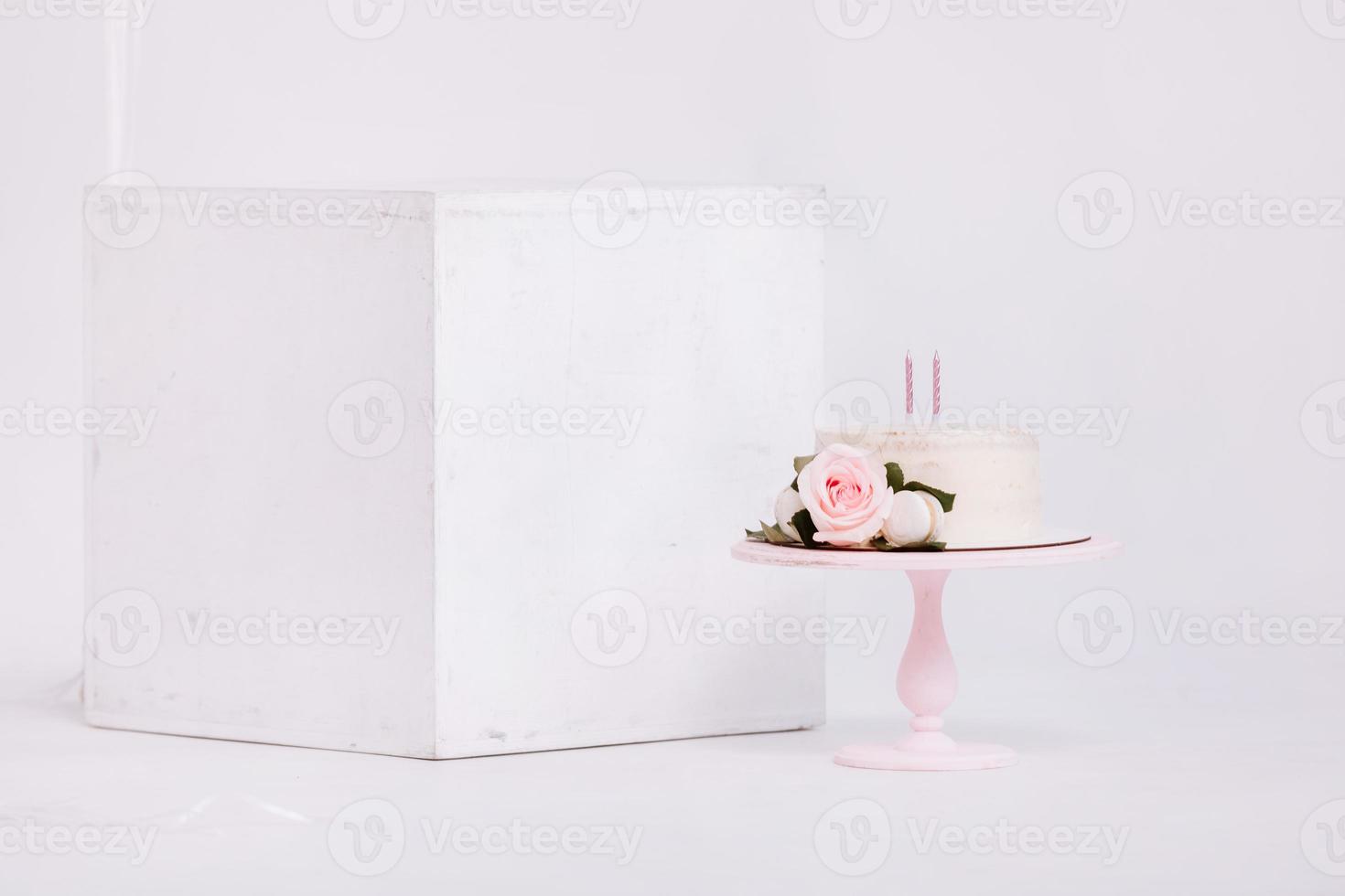 Beautiful white cream cake decorated with 2 year old candle and roses in white studio. Birthday party - Concept of a year of birth, party, celebration of life and memorable moments. photo