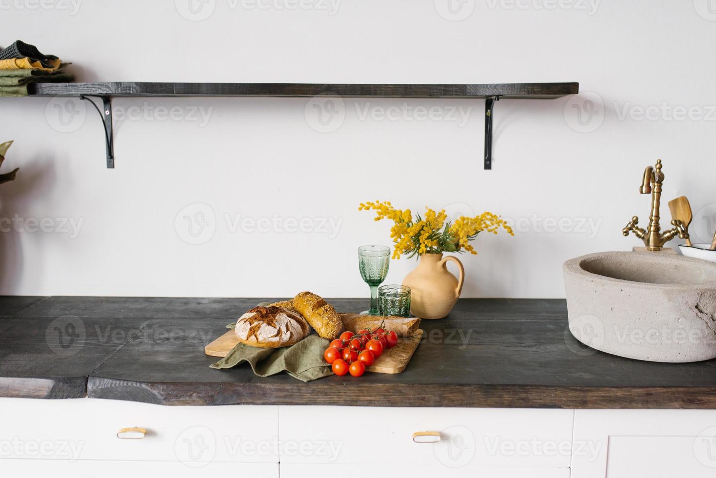 Bright, modern kitchen with stone sink. Loaves of fresh homemade bread and a sprig of tomato on a chopping board, mimosa in a clay vase. decor in the Scandinavian kitchen photo