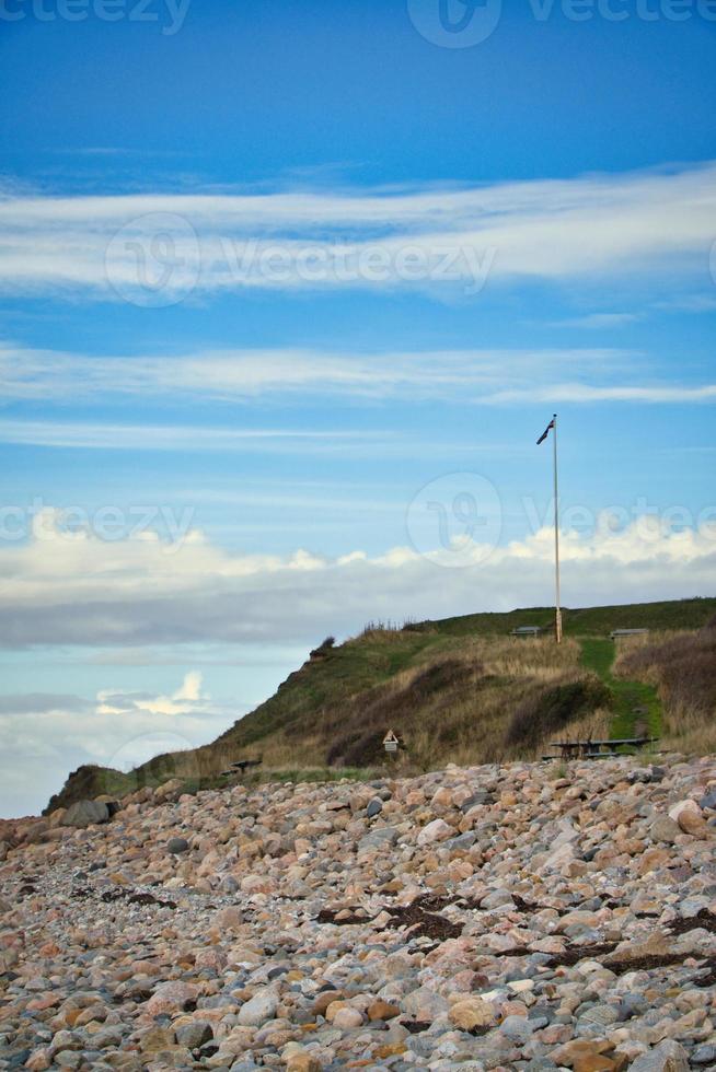 Stone beach by the sea. Flagpole with Danish flag on a hill. Danish coast photo