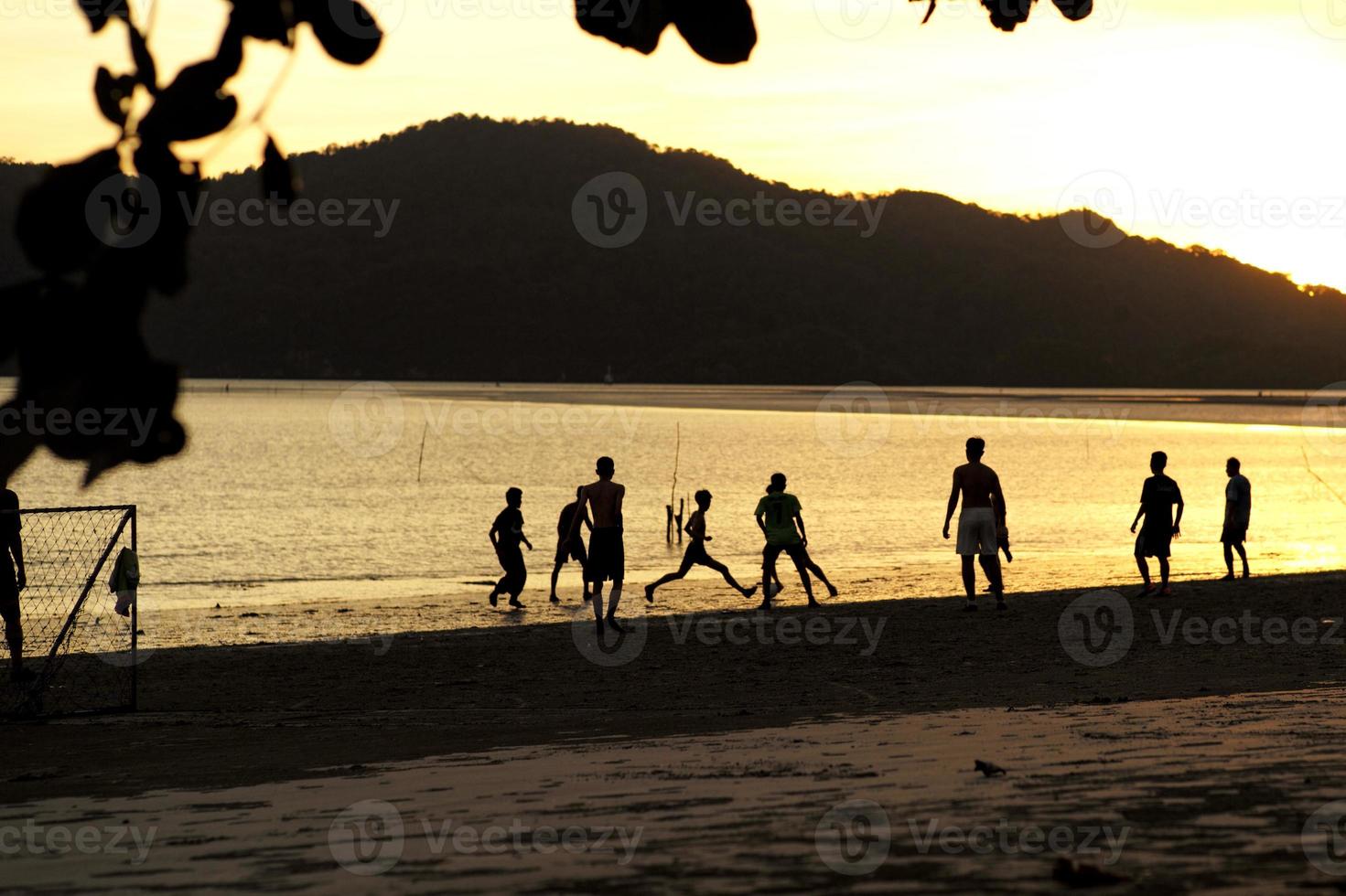 Silhouette group of people playing the football on the beach in the sunset with seascape and mountain in background photo