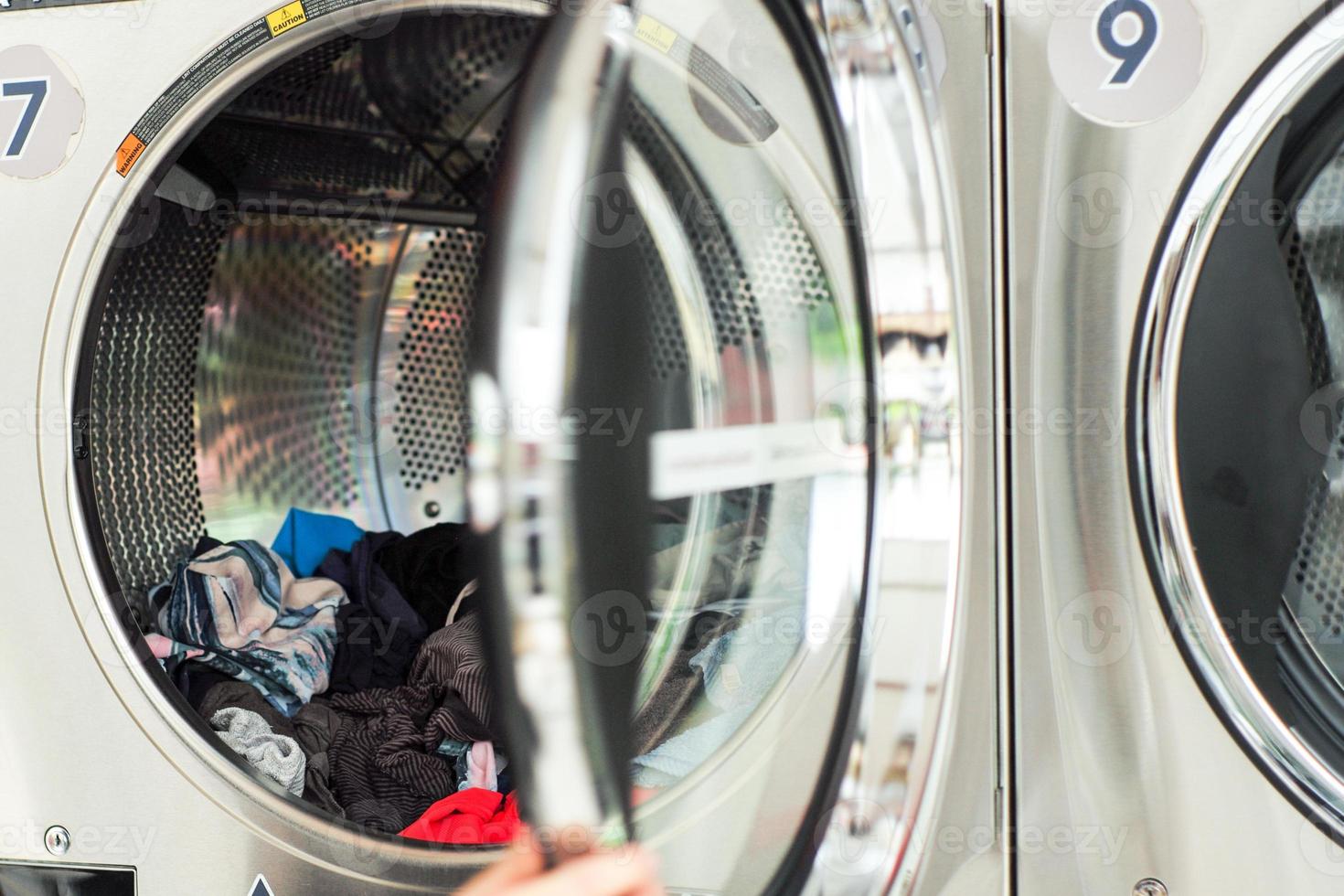 Selective focus on the pile of clothes inside the dry machine with blurred front door in foreground photo
