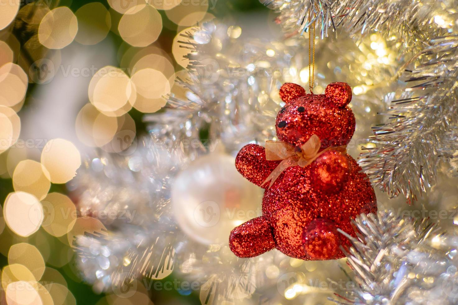 Selective focus on the right eye of the teddy bear doll decorated on the Christmas tree with glittering bokeh lights in background photo