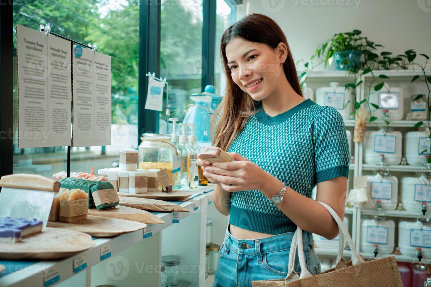 A young Caucasian woman chooses and shops for reusable and recycled appliance products, soap in refill store, zero-waste grocery, and plastic-free, environment-friendly, sustainable lifestyle. photo