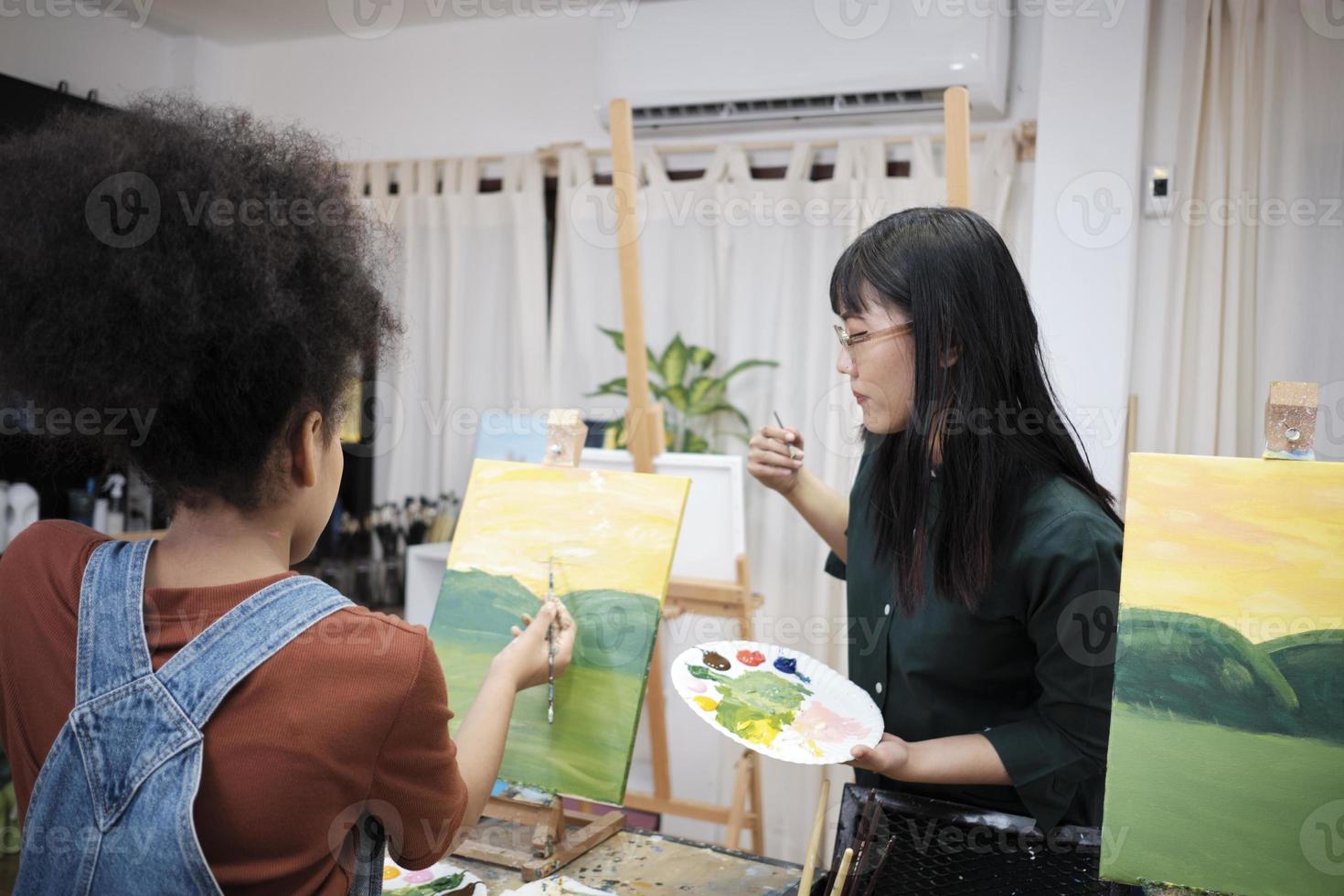 Female Asian teacher teaches and demonstrates to a student girl on acrylic color picture painting on canvas in art classroom, creatively learning with skill at the elementary school studio education. photo