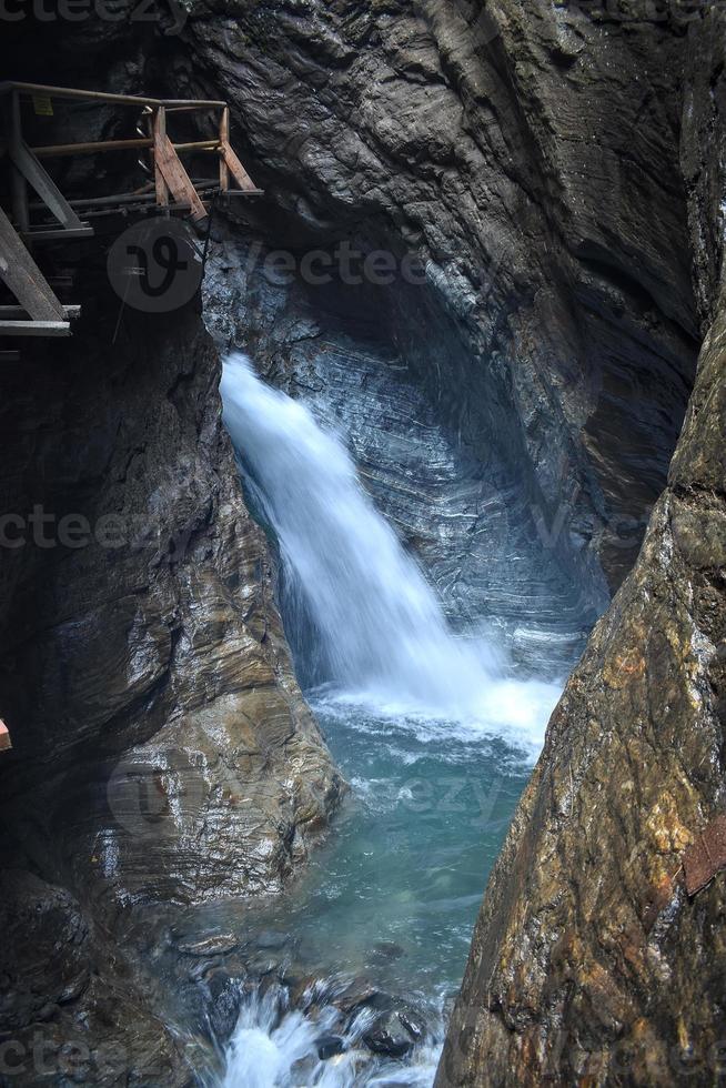 Beautiful waterfall in a cave in a ravine called Raggaschlucht with a wodden bridge or hiking trail on the left. Wild nature in Austria. photo