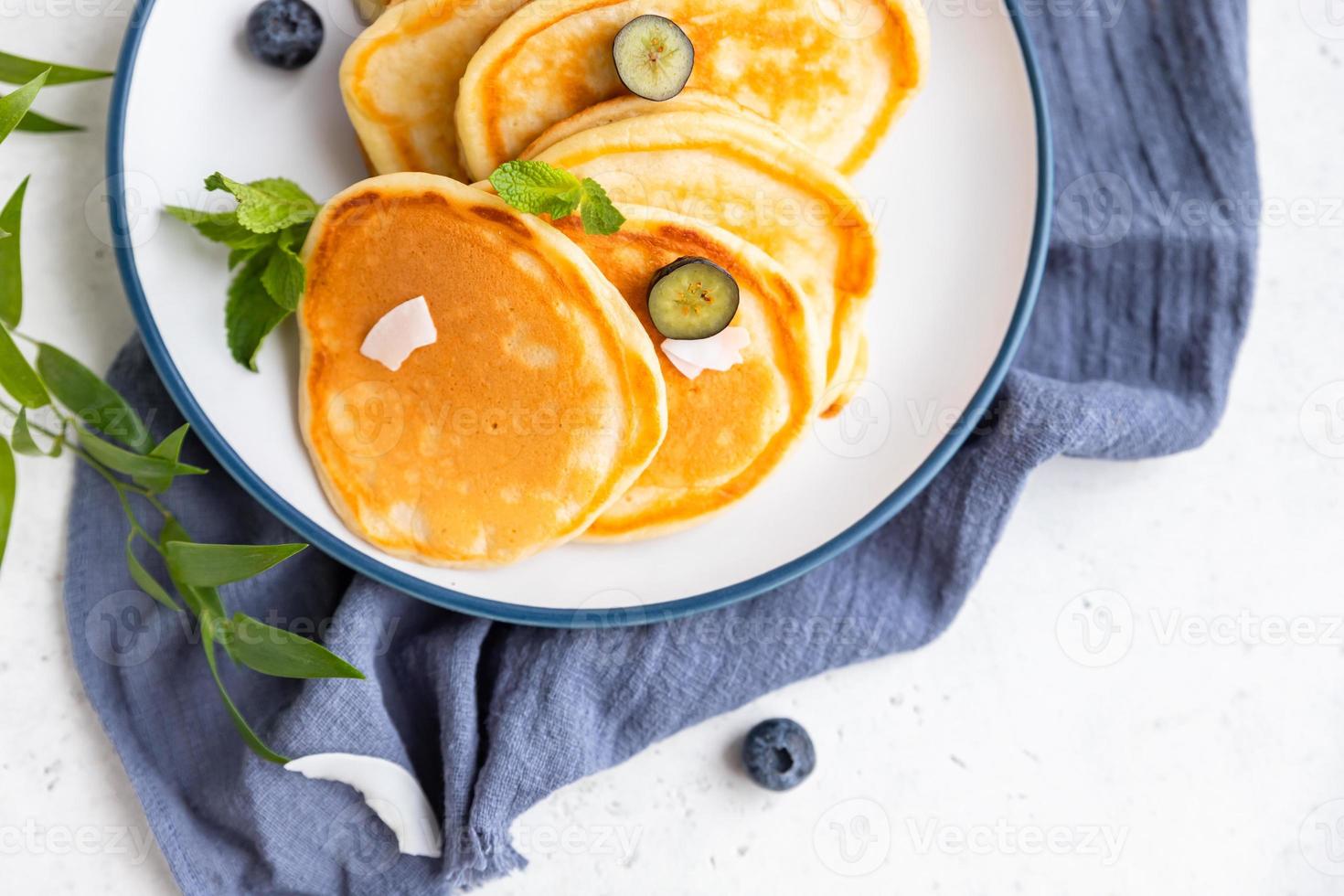 Traditional fluffy pancakes with orange jam, blueberries, coconut chips and mint for healthy breakfast, light background. High key photography. photo