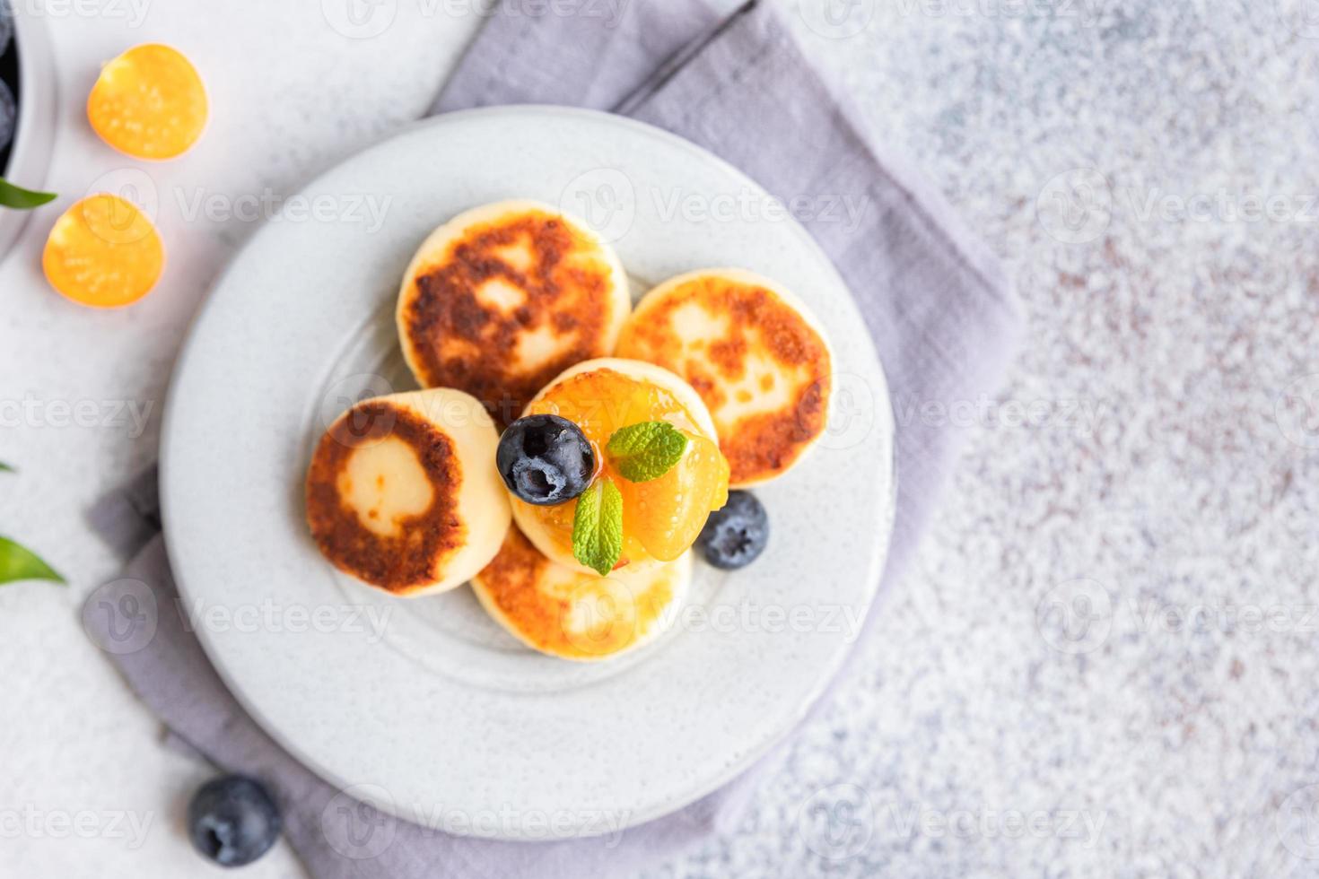 tortitas de requesón, buñuelos de cuajada dulce con arándanos y physalis, fondo de hormigón. syrniki con mermelada y bayas para un desayuno saludable. foto