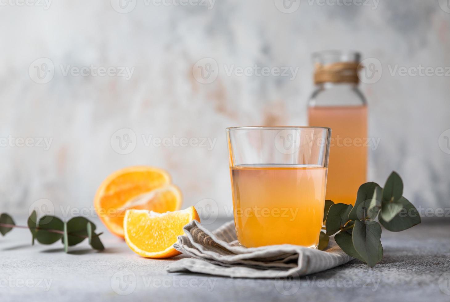 Orange lemonade in glass and bottle with fresh orange, concrete background. Refreshing drink. Cocktail bar background concept. photo