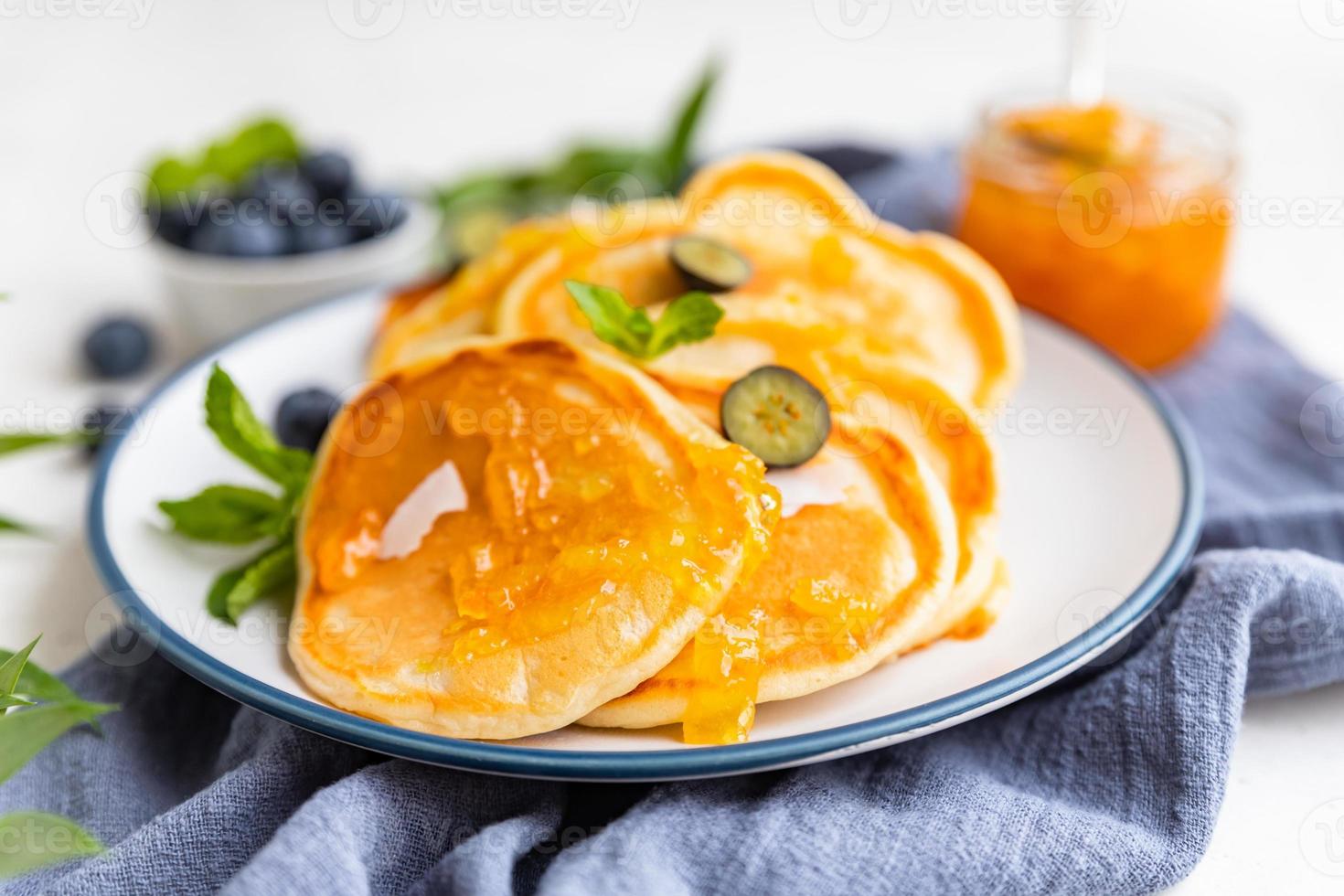 Traditional fluffy pancakes with orange jam, blueberries, coconut chips and mint for healthy breakfast, light background. High key photography. photo