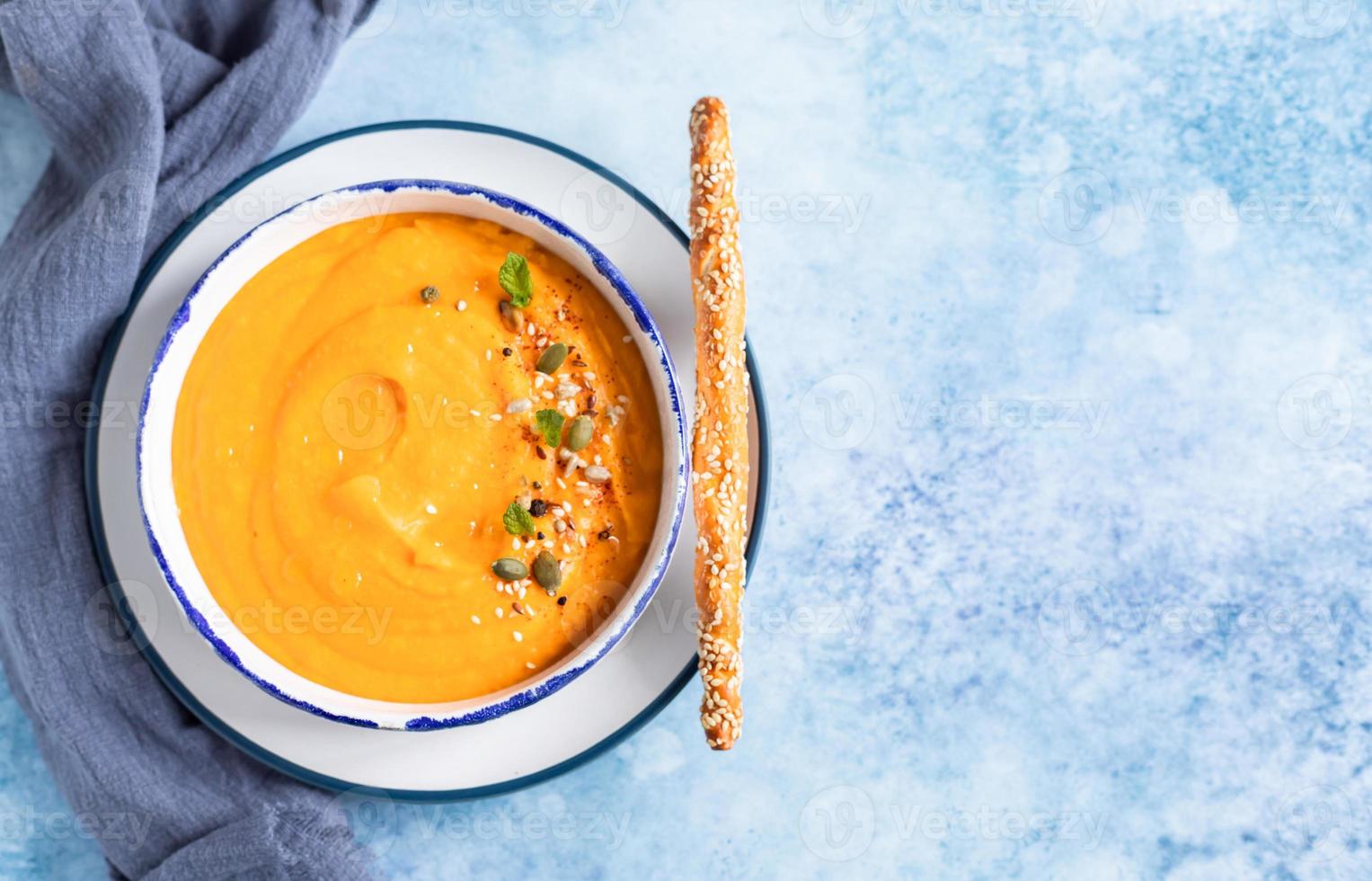 Bright vegetarian autumn pumpkin and carrot soup with seeds, mint and spices, blue background. Comfort food, fall and winter healthy slow food concept. photo