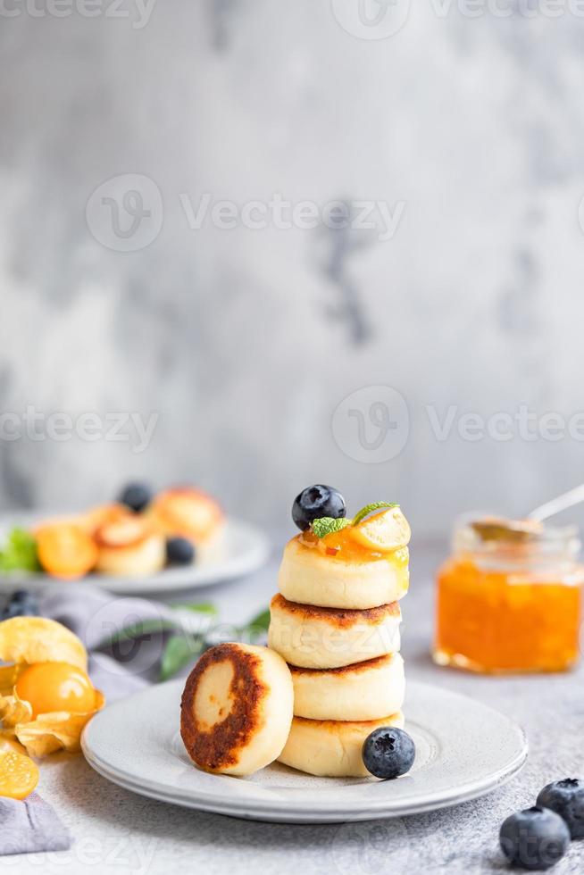 tortitas de requesón, buñuelos de cuajada dulce con arándanos y physalis, fondo de hormigón. syrniki con mermelada y bayas para un desayuno saludable. foto