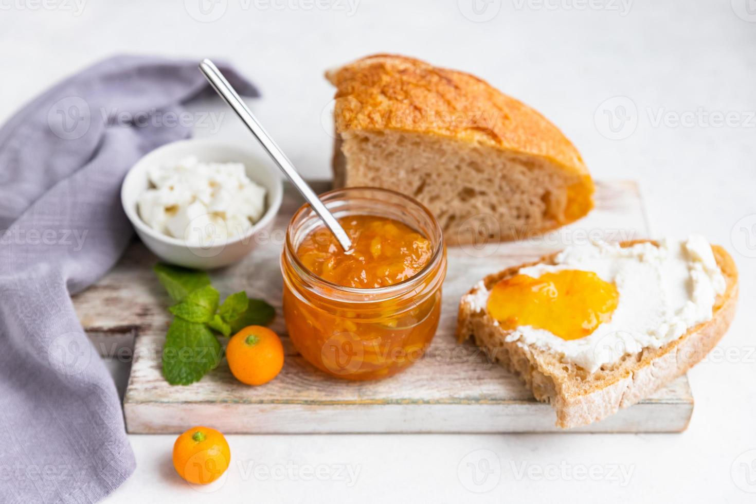 Sliced artisan homemade bread with ricotta or cottage cheese and orange jam on light background. Tasty breakfast. High key photography. photo