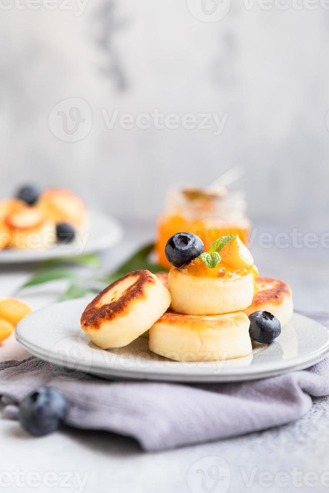 tortitas de requesón, buñuelos de cuajada dulce con arándanos y physalis, fondo de hormigón. syrniki con mermelada y bayas para un desayuno saludable. foto