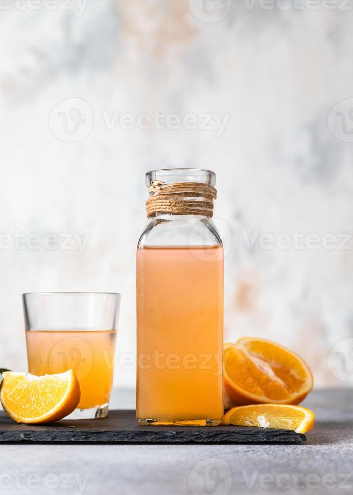 Orange lemonade in glass and bottle with fresh orange, concrete background. Refreshing drink. Cocktail bar background concept. photo