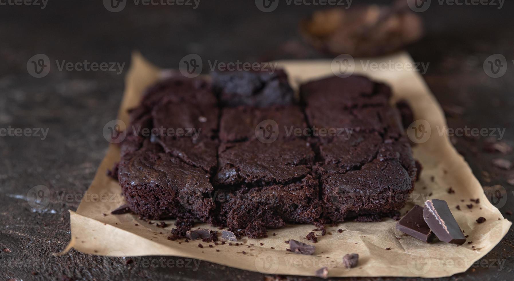 Chocolate spongy brownie cakes on brown baking paper with pieces of dark chocolate and cocoa powder, brown background. photo
