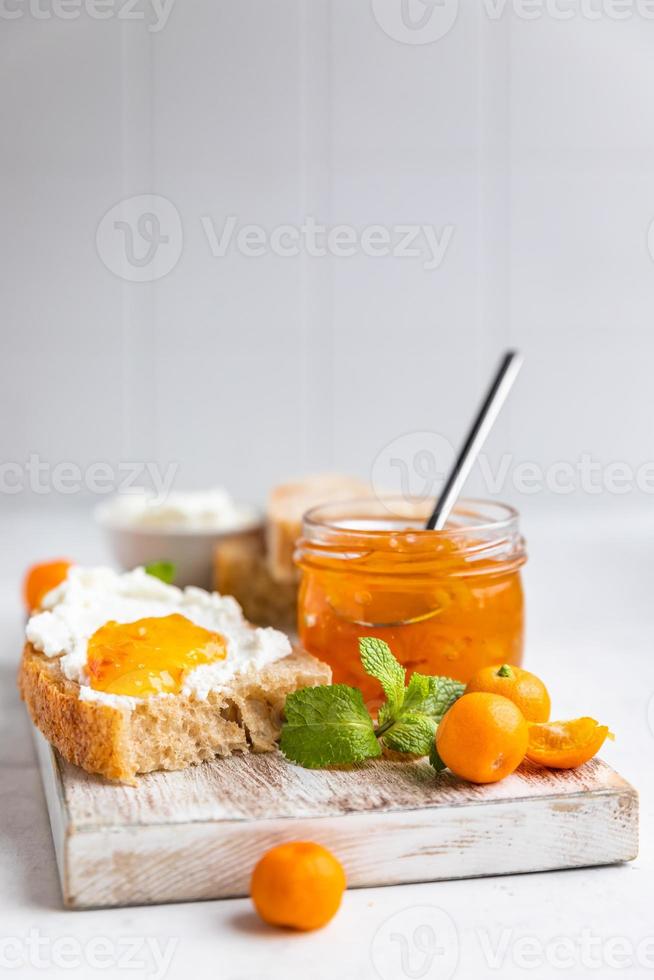 Sliced artisan homemade bread with ricotta or cottage cheese and orange jam on light background. Tasty breakfast. High key photography. photo
