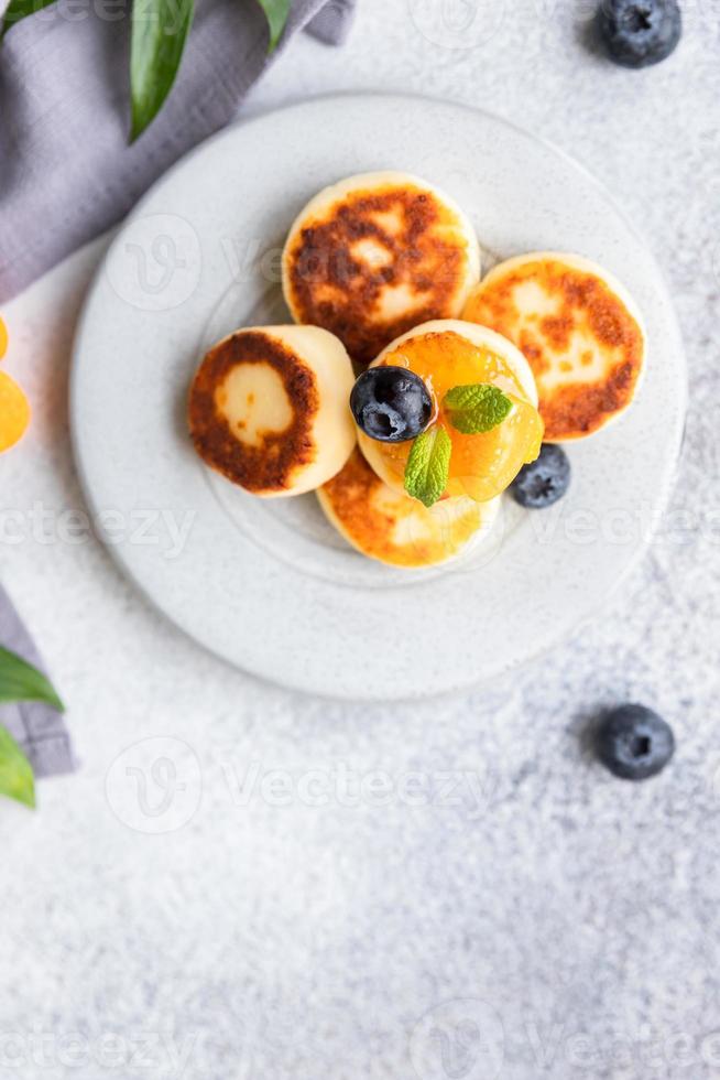 tortitas de requesón, buñuelos de cuajada dulce con arándanos y physalis, fondo de hormigón. syrniki con mermelada y bayas para un desayuno saludable. foto