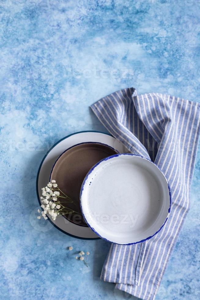 Handmade ceramic white plates with blue stripe on the edge and dried flowers on blue concrete background. Top view. photo