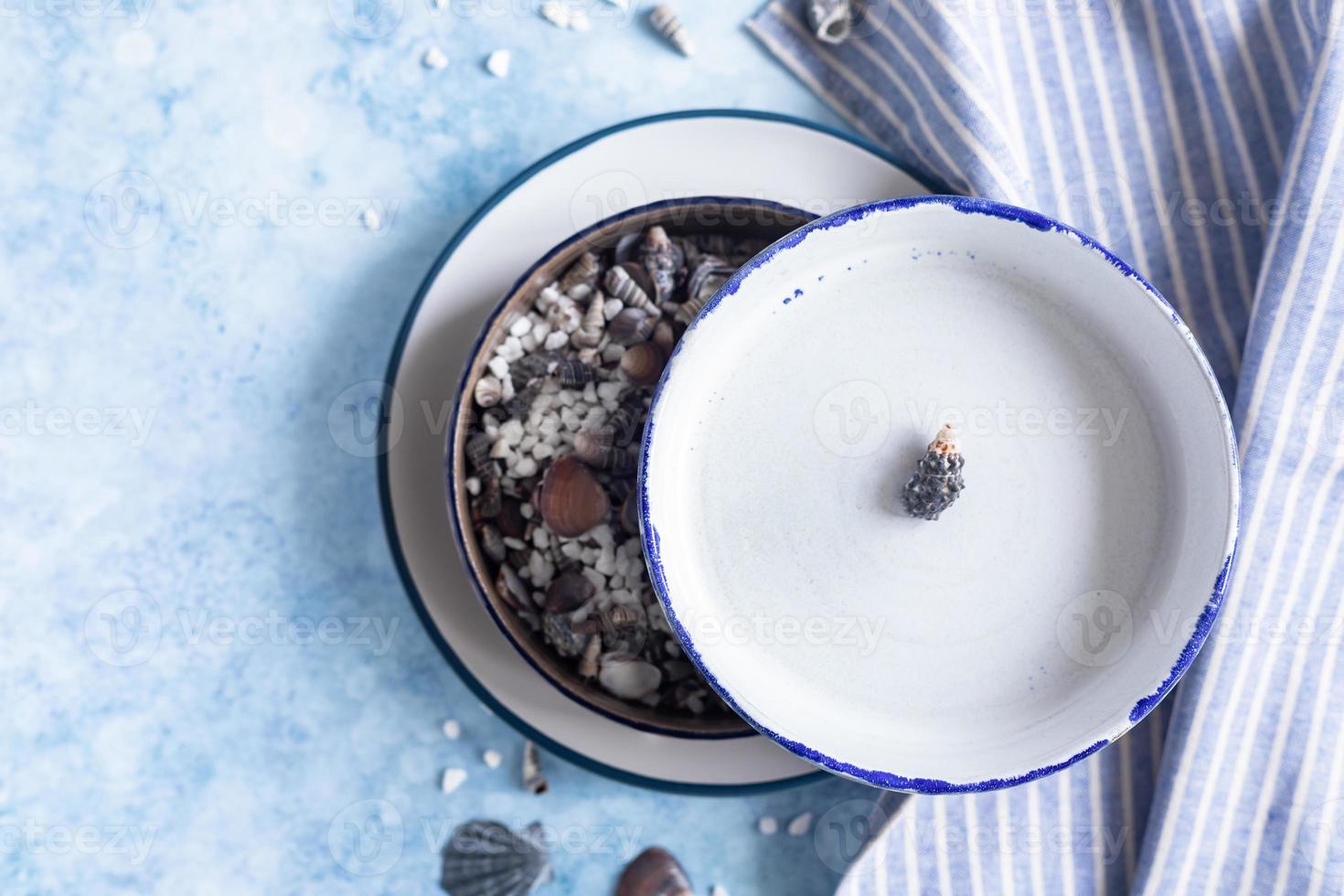 Handmade ceramic white plates with blue stripe on the edge and empty seashells on blue concrete background. Top view. photo
