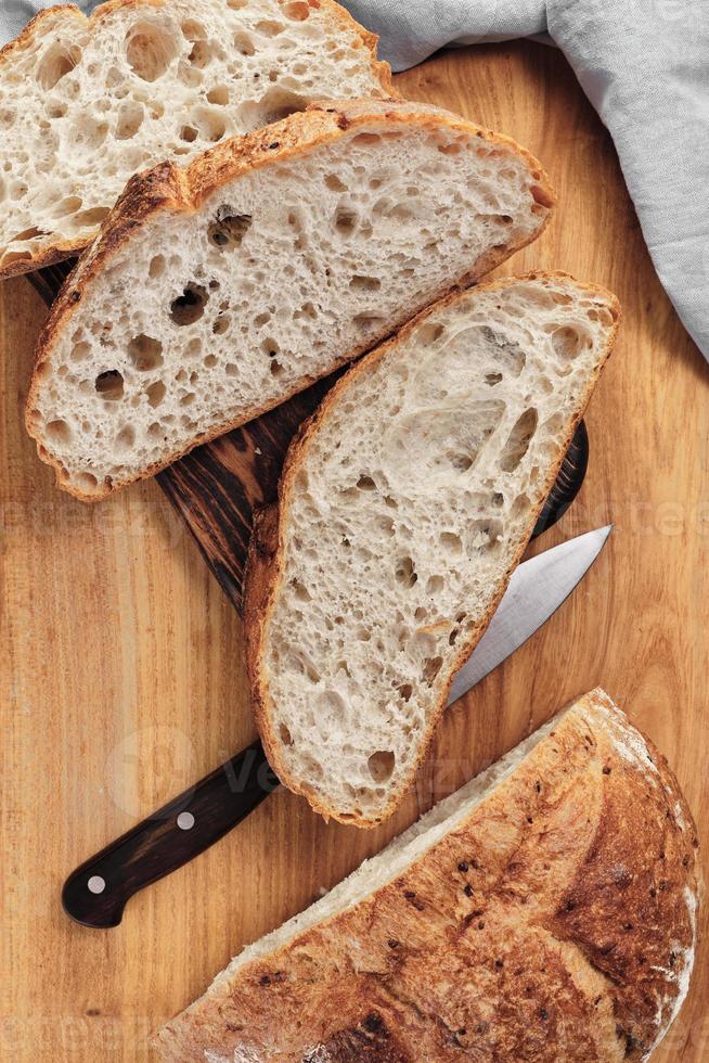Sliced round rustic bread without kneading on a cutting board next to a knife. Homemade whole grain bread, layout on the table, vertical frame photo