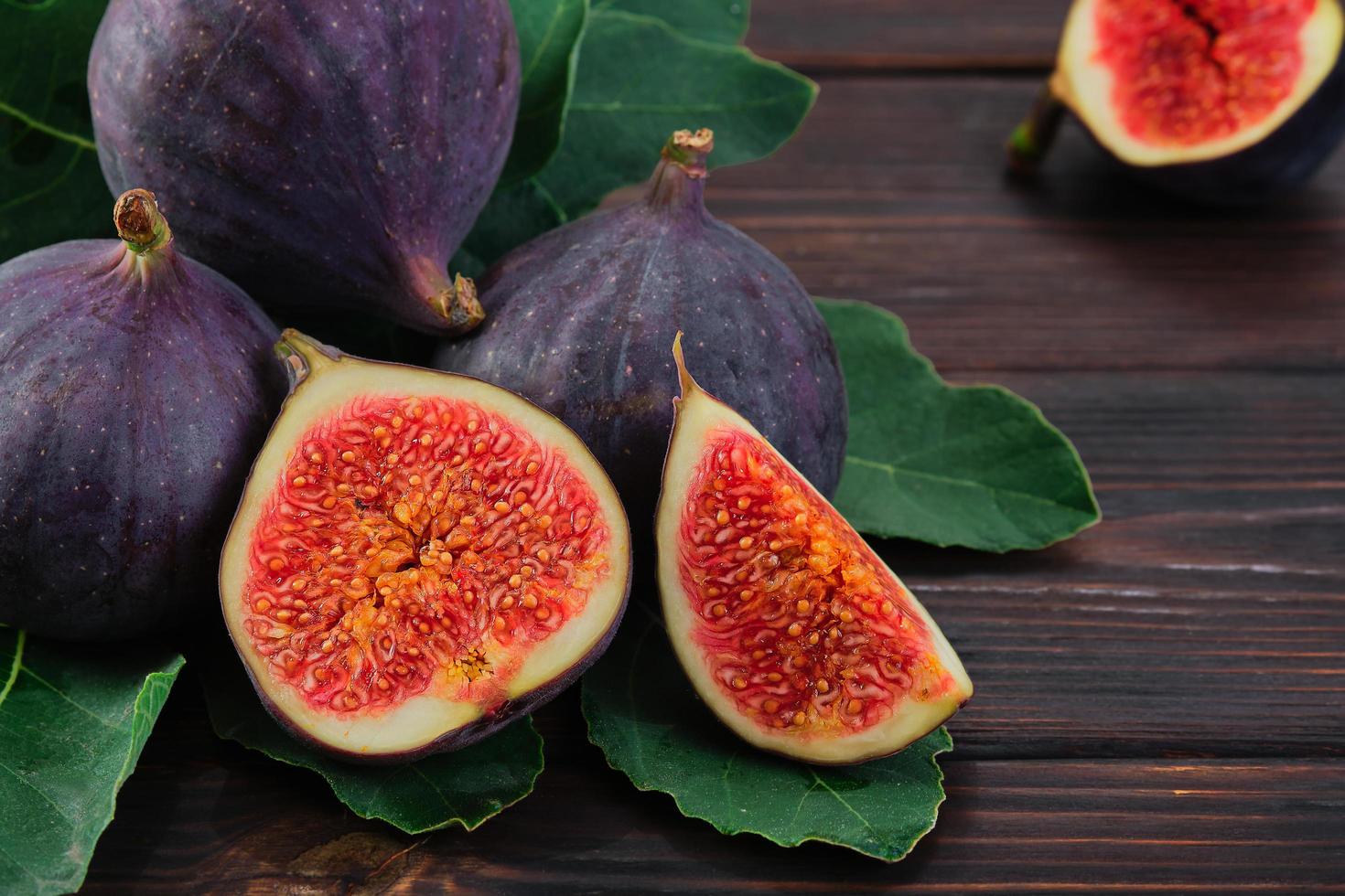 Figs and halves of several fruits close-up on the leaves of a fig tree on an old wooden table, horizontal frame. Seasonal fruits, fig harvest background or mediterranean diet articles photo