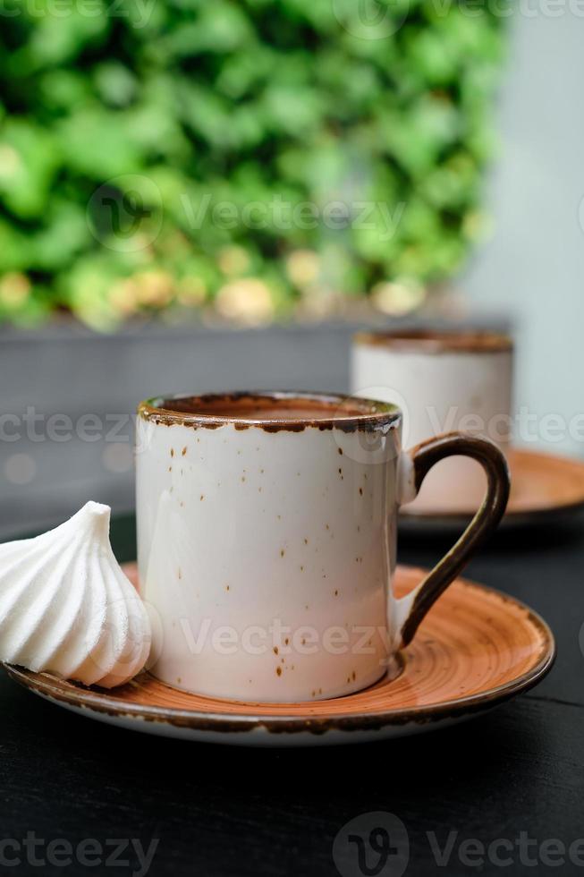 Cup of Turkish black frothy coffee on a black stone table with branches of wild ivy in the background, bizet next to the cup. Vertical frame, selective focus photo