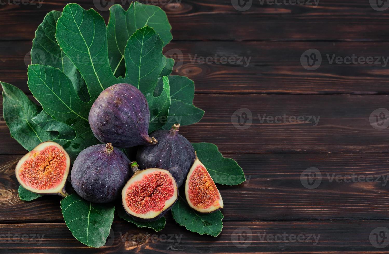 Figs and halves of several fruits on fig tree leaves on an old wooden table, horizontal frame with copy space. Seasonal fruits, fig harvest background or mediterranean diet articles photo