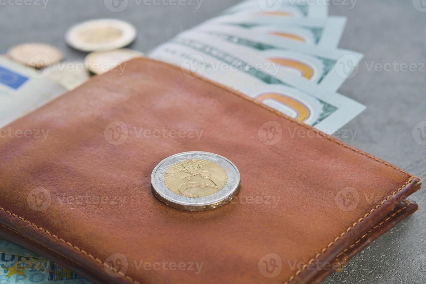 Euro coin and us dollar banknotes in a brown leather wallet on a gray table background, close-up, selective focus, blurred background, business finance concept photo