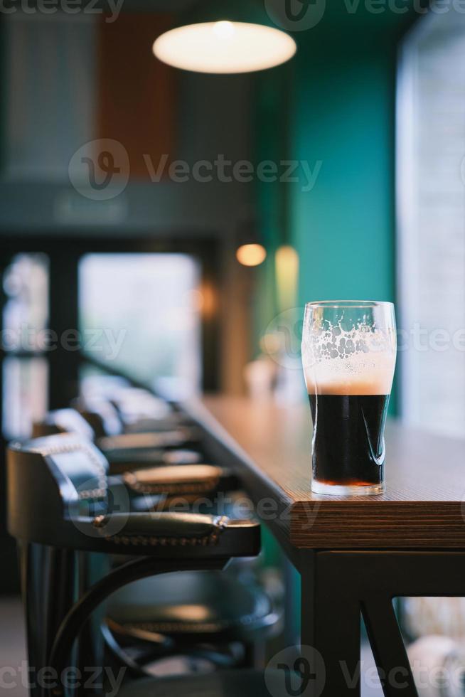 Vertical shot, close-up on a glass of beer on the bar counter, selective focus. Bar view, blur focus, bar decoration idea or photo for interior