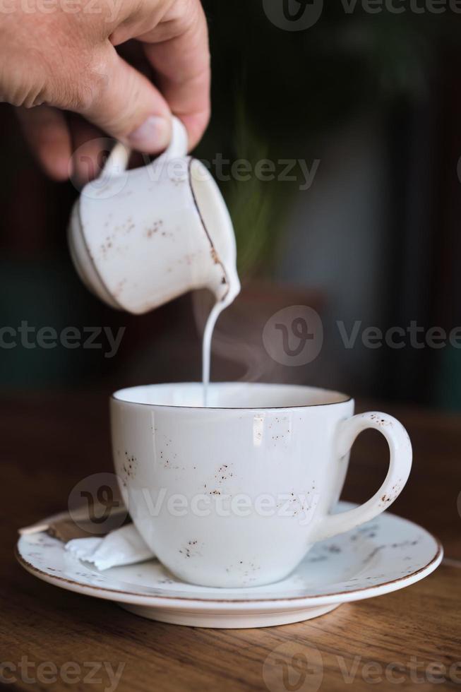 Barista pouring milk into a cup of coffee, vintage color photograph, film noise and grain in photograph. Vertical frame, selective focus. Idea for screensaver or menu, articles about coffee photo